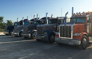 Five different colored bulk liquid transporting trucks line up on a gravel road