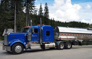 Liquids in Motion blue and silver bulk liquid hauling truck on paved road in front of trees 