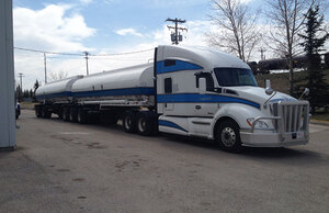 Liquids in Motion white and blue bulk liquid hauling truck on paved road. 