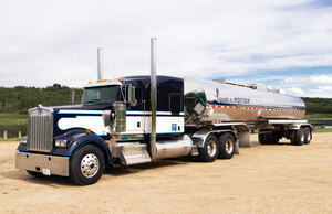 Liquids in Motion blue, white, and silver bulk liquid hauling truck on gravel road in front of a lake. 