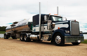 Liquids in Motion blue, white, and silver bulk liquid hauling truck on gravel road in front of a lake. 