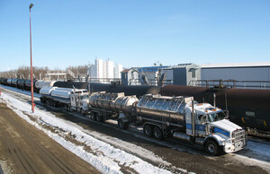 Two white and blue Liquids in Motion bulk liquid moving trucks parked beside a train