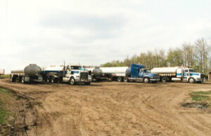 Old image of multiple water transport trucks lined up on a gravel road